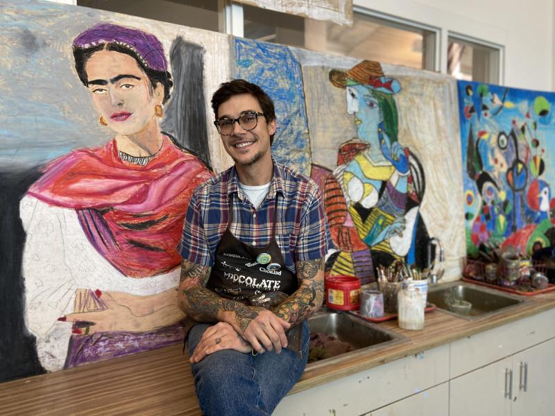 Second-year Love Creek Elementary art teacher Forest Allread poses with murals painted by students in a collaborative project. A working artist himself, Allread manages his class under the teaching for artistic behavior model, in which students are responsible for their own learning. ELLEN DRISCOLL PHOTO